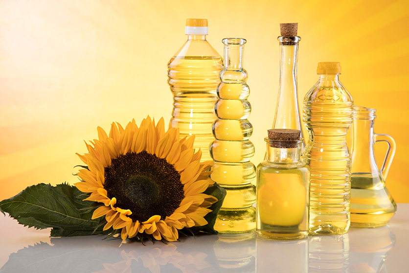 A sunflower placed next to several types of bottles of cooking oil