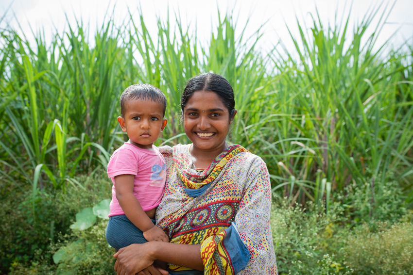 Smiling Woman Carrying Child in A Green Field