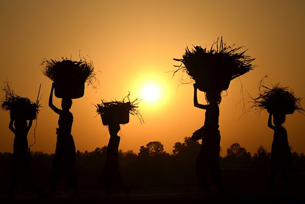 Farmers carrying baskets of harvest on their heads at sunset