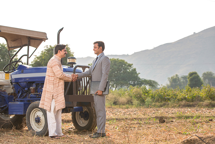 A farmer and corporate person shaking hands in a field