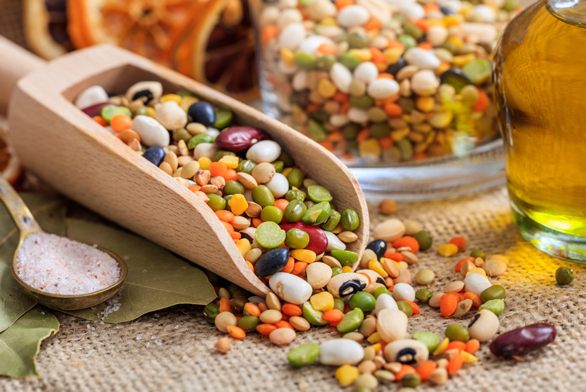 Wooden spoon with mixed pulses next to a jar of mixed pulses and a bottle of oil