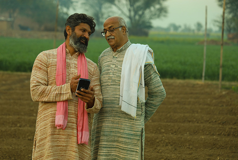 Two farmers in a field talking over something on a phone screen