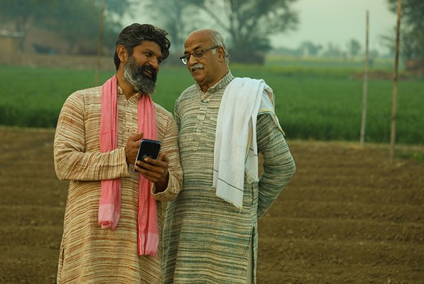 Two farmers in a field talking over something on a phone screen