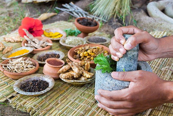 Hands preparing paste in mortar and pestle next to several herbs