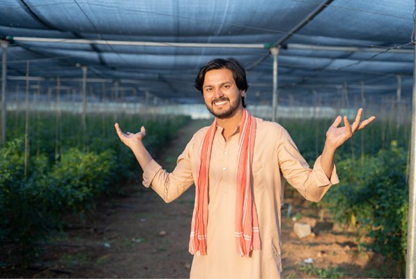 Picture of happy smiling farmer showing greenhouse with both hands.