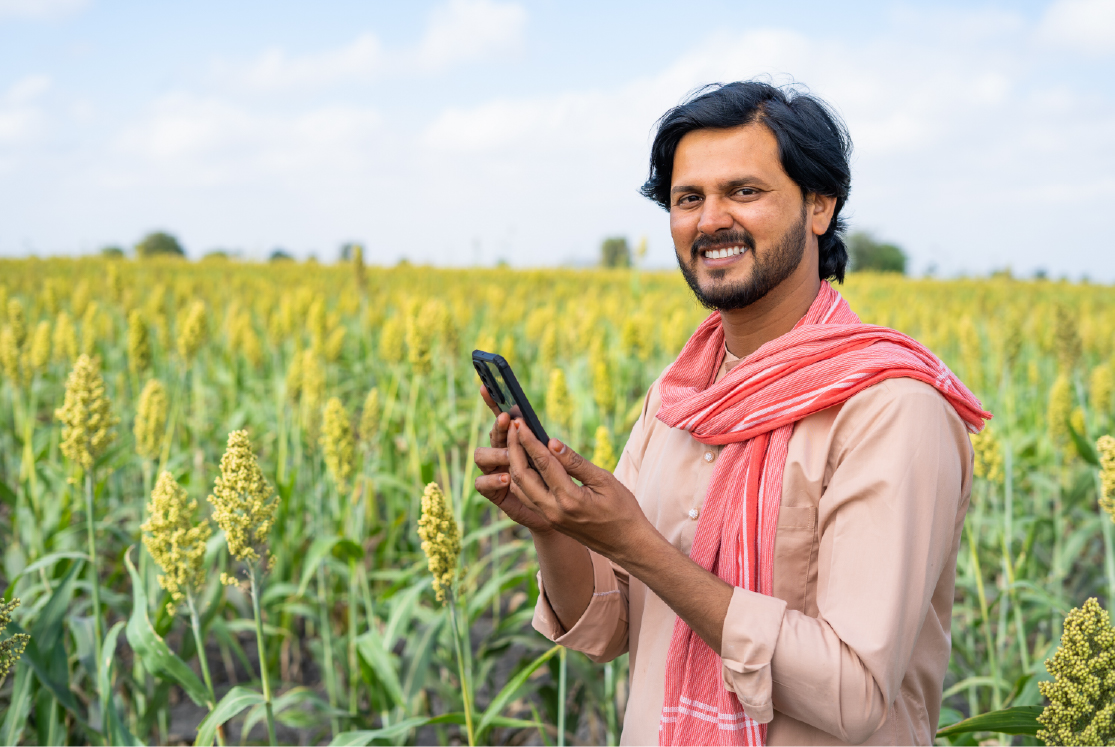Smiling farmer with mobile phone at agricultural farm land.