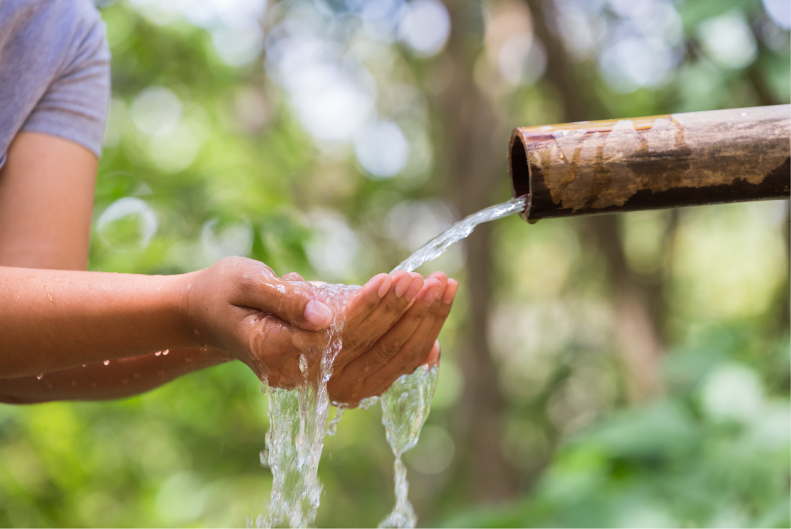 Person cupping their hands to gather water under a flowing water pipe