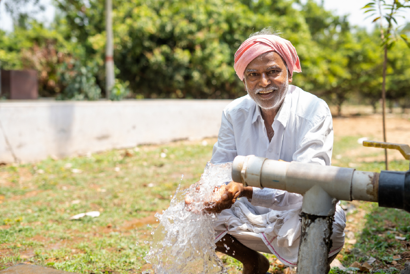 Happy Indian farmer gathering water in both hands from a borewell pipe at farmland