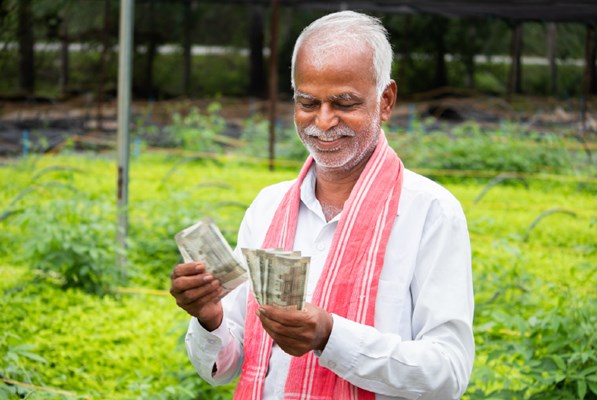 Happy Indian farmer counting currency notes in a green field