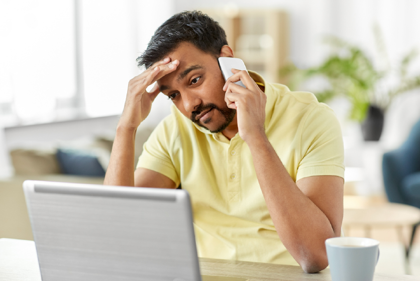 Indian man calling on smartphone in front of a laptop