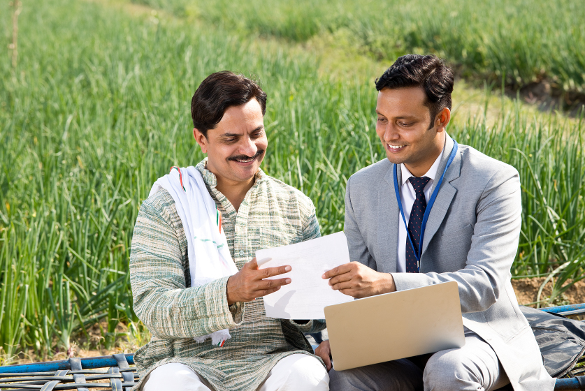 Indian farmer with businessman using laptop on agriculture field