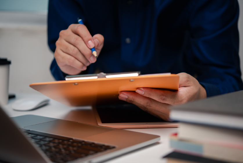 Man holding clipboard with checklist in front a laptop in a workplace