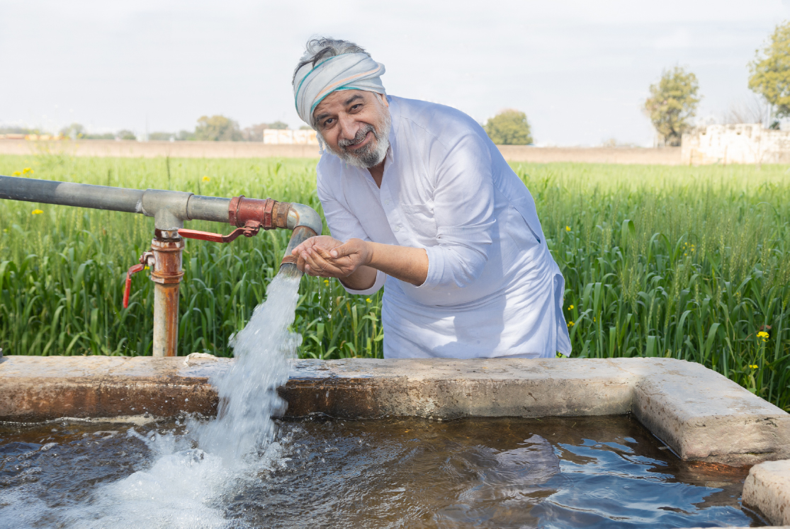 Happy Indian farmer drinking fresh water from tube well irrigation pipe in an agricultural field
